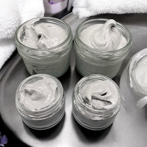 Puede incluir: Cuatro tarros de vidrio llenos de una sustancia cremosa gris. Los tarros están en una bandeja plateada.