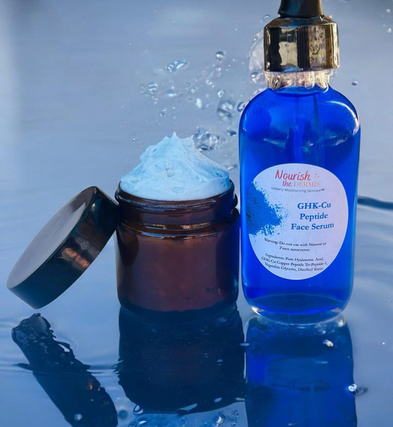May include: A blue glass bottle with a dropper top and a white label that reads "Nourish the Dermis" and "GHK-Cu Peptide Face Serum". The bottle is sitting on a blue surface with water droplets. A brown glass jar with a white cream inside is also on the surface.