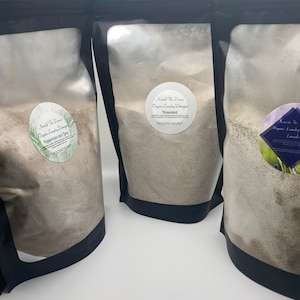 May include: Three black pouches filled with laundry detergent. Each pouch has a round label with text. The labels read "Nourish The Damis Organic Laundry Detergent" with different scents: Peppermint and Lime, Unscented, and Lavender Tea.