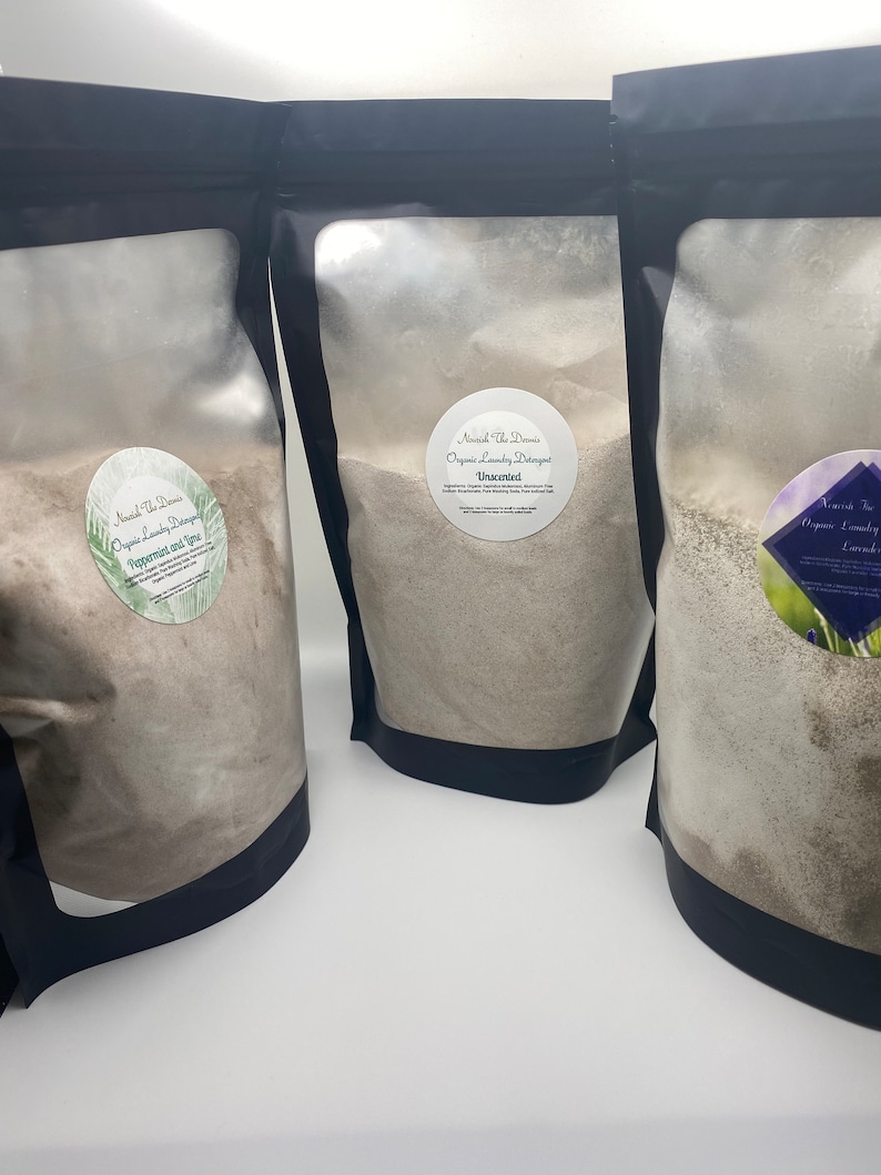 May include: Three black pouches filled with laundry detergent. Each pouch has a round label with text. The labels read "Nourish The Damis Organic Laundry Detergent" with different scents: Peppermint and Lime, Unscented, and Lavender Tea.