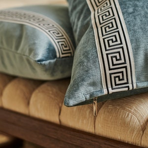 May include: Two blue throw pillows with white and black geometric patterns on a beige tufted bench.