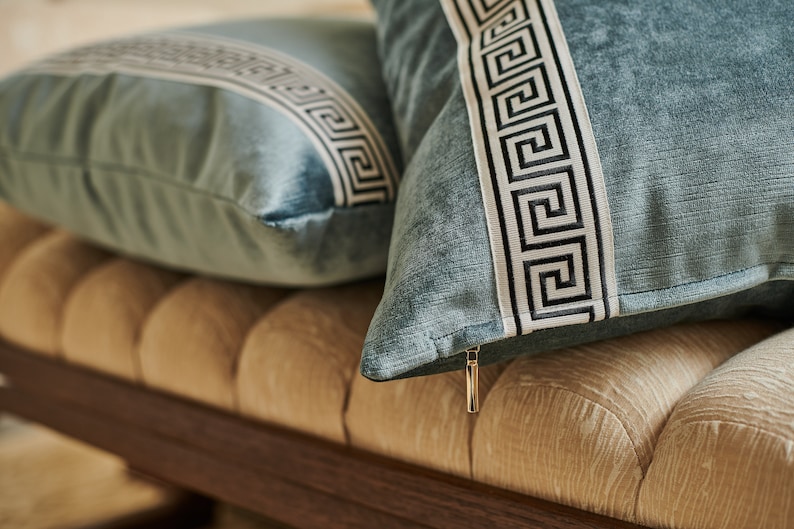 May include: Two blue throw pillows with white and black geometric patterns on a beige tufted bench.
