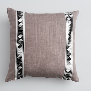 May include: A mauve-colored throw pillow with a white and black Greek key pattern border.
