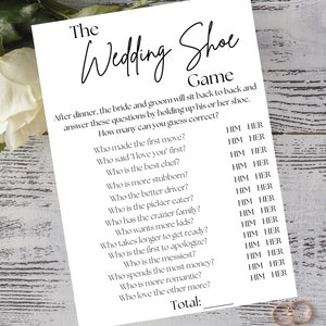 May include: A white wedding game card titled "The Wedding Shoe Game" with questions like "Who made the first move?" and "Who said 'I love you' first?" Gold wedding rings are in the bottom right corner.