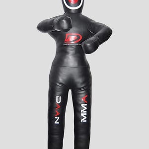 May include: Black MMA training dummy with a red and white target on the head. The dummy has a Daan MMA logo on the torso and the words Daan and MMA printed on the legs. The dummy is designed for martial arts training.