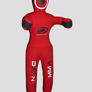 May include: Red and black MMA training dummy. The dummy is in the shape of a human body with arms outstretched. The head has a white circle around a black centre. The text "DAAN MMA" is printed on the legs, and the website address is printed on the back.