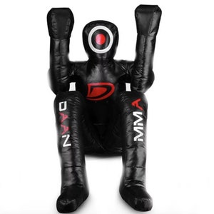 May include: Black freestanding punching bag with red and white markings. The bag is shaped like a person and has the words "DAAN" and "MMA" printed on the legs.