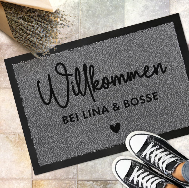 May include: A grey welcome mat with black text that reads "Willkommen bei Lina & Bosse" with a small black heart.