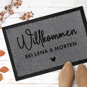 May include: A grey welcome mat with black text that reads "Willkommen bei Lena & Morten" with a small black heart symbol.