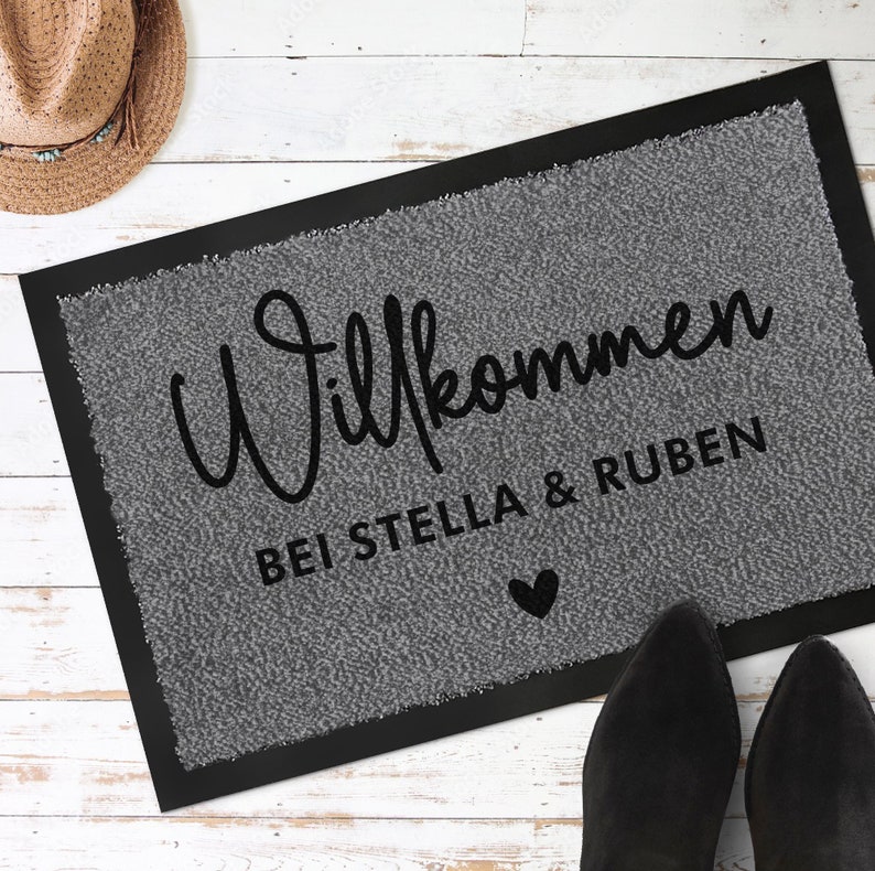 May include: Grey welcome mat with black text that reads "Willkommen bei Stella & Ruben" with a small black heart.