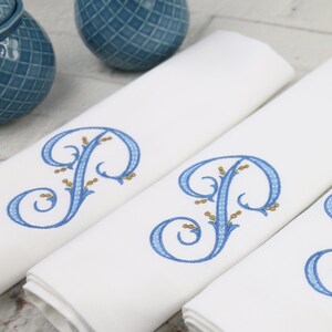 May include: Four white linen napkins with blue and gold embroidered initial "P" in a decorative script.