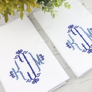 May include: Two white kitchen towels with blue and light blue embroidered monograms in a decorative script font. The monogram is "KJM".