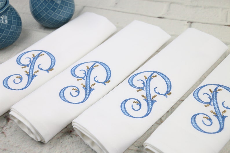 May include: Four white linen napkins with blue and gold embroidered initial "P" in a decorative script.