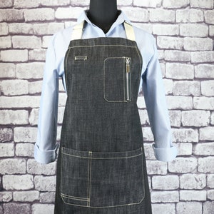 May include: A black denim apron with a zippered pocket and a large lower pocket. The apron has adjustable straps and is made of durable denim.