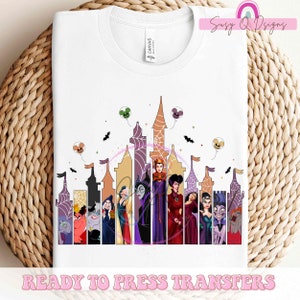 May include: White t-shirt featuring a colorful graphic of Disney villains in front of a castle silhouette. The design includes bats, Mickey Mouse balloons, and the text "READY TO PRESS TRANSFERS".