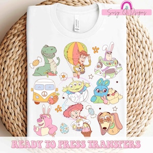 May include: A white t-shirt with a colorful design featuring characters from the Toy Story franchise. The design includes Woody, Buzz Lightyear, Rex, Jessie, and other characters. The design is perfect for fans of the Toy Story movies.