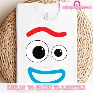 May include: White t-shirt featuring a cartoon face design with red, blue, and black accents. The design includes a red wavy line, two eyes, and a blue smile. The text "READY TO PRESS TRANSFERS" is at the bottom.