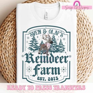May include: White t-shirt with a blue and white design featuring a reindeer, Sven, and Olaf from the movie Frozen. The design includes the text "Sven & Olaf's Reindeer Farm Est. 2013".