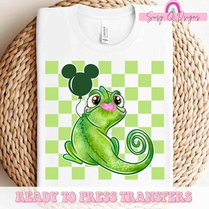 May include: A green chameleon with a pink tongue holding a black Mickey Mouse balloon. The chameleon is on a green and white checkered background.  Ready to Press Transfers.