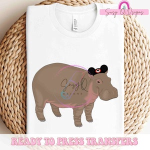 May include: A white t-shirt with a brown hippopotamus wearing a black Mickey Mouse ears hat. The text "Suzy Q Designs" is in the top right corner of the image. The text "Ready to Press Transfers" is at the bottom of the image.