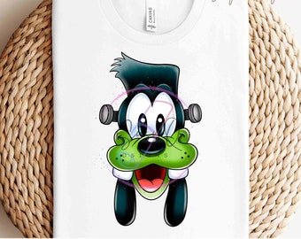 Könnte beinhalten: Weißes T-Shirt mit einem Cartoon-Charakter-Design. Das Design zeigt einen grüngesichtigen Charakter mit schwarzen Haaren und Schrauben, der dem Monster von Frankenstein ähnelt. Die Figur hat große Augen und einen lächelnden Mund. Der Text "READY TO PRESS TRANSFERS" steht unten.