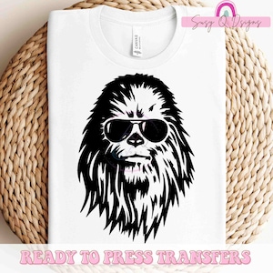 May include: A white t-shirt with a black and white graphic of a furry creature wearing sunglasses. The text "READY TO PRESS TRANSFERS" is at the bottom of the shirt.