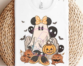 Könnte beinhalten: Weißes T-Shirt mit einem Halloween-Design. Die Grafik zeigt einen Geistercharakter mit Minnie-Maus-Ohren und einer gepunkteten Schleife, der einen Kürbis-Laterne hält. Fledermäuse, Grabsteine und Kürbisse ergänzen das Design. Der Text "READY TO PRESS TRANSFERS" befindet sich unten.