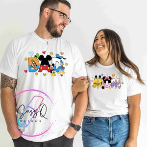 May include: White t-shirts with a Disney theme. The shirt on the left says "DAD" with Mickey Mouse, Donald Duck, and Goofy characters. The shirt on the right says "MOM" with Minnie Mouse, Pluto, and Daisy Duck characters.