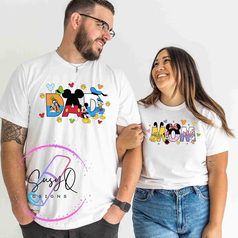 May include: White t-shirts with a Disney theme. The shirt on the left says "DAD" with Mickey Mouse, Donald Duck, and Goofy characters. The shirt on the right says "MOM" with Minnie Mouse, Pluto, and Daisy Duck characters.