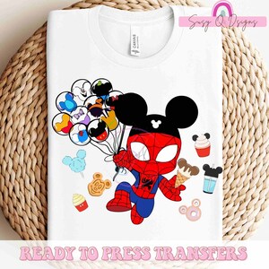 May include: A white t-shirt with a design of a cartoon Mickey Mouse dressed as Spiderman holding balloons with Disney characters on them. The design also includes various Disney-themed treats like ice cream, donuts, and cotton candy. The text "READY TO PRESS TRANSFERS" is at the bottom of the shirt.