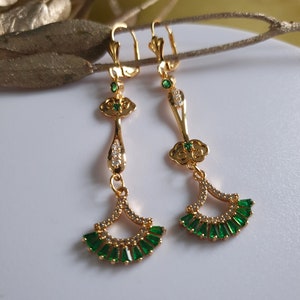 Op de afbeelding: Gouden oorhangers met groene en witte stenen. De oorbellen hebben een waaiervormig ontwerp met een wolkvormige hanger boven de waaier.