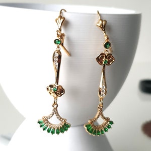 Op de afbeelding: Gouden oorhangers met groene en heldere kristallen accenten. De oorbellen hebben een wolkontwerp en een waaiervormige onderkant.