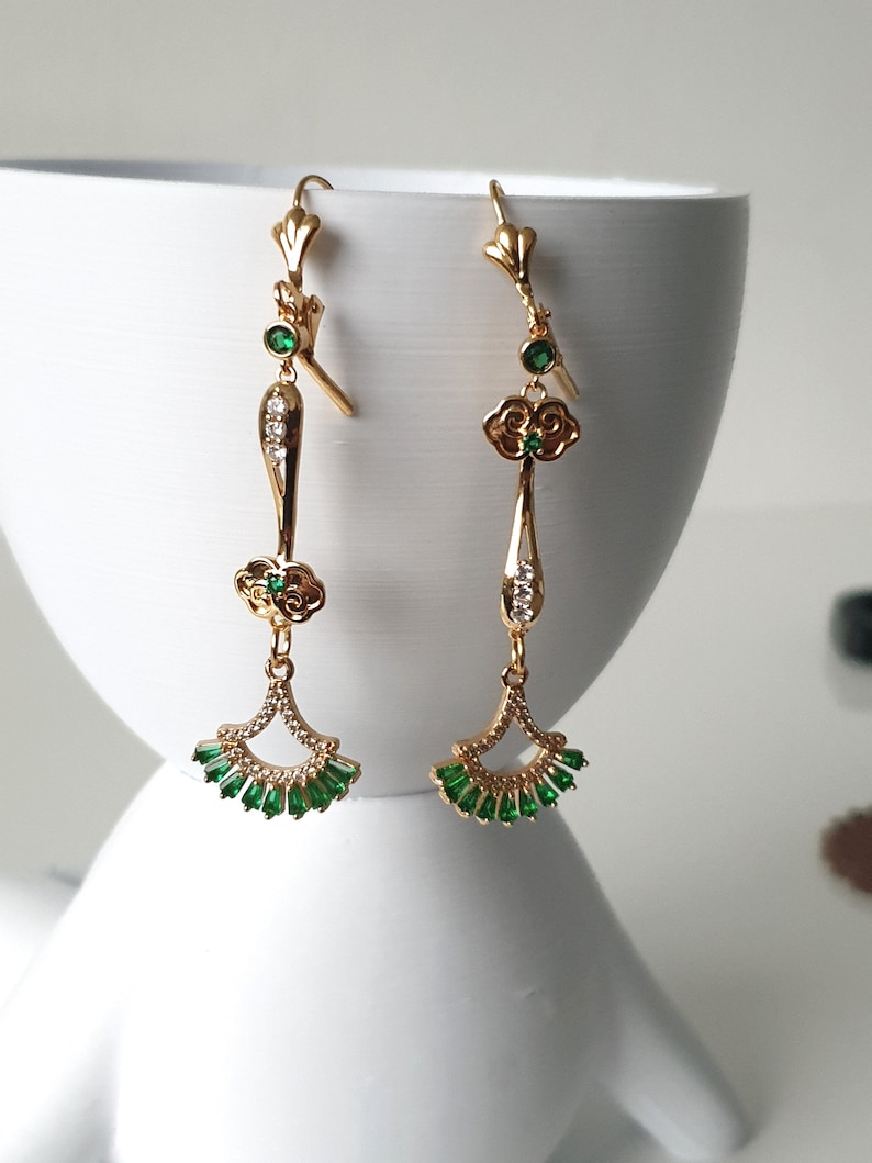 Op de afbeelding: Gouden oorhangers met groene en witte stenen. De oorhangers hebben een waaiervormig ontwerp met een klein bloemetjesdetail.