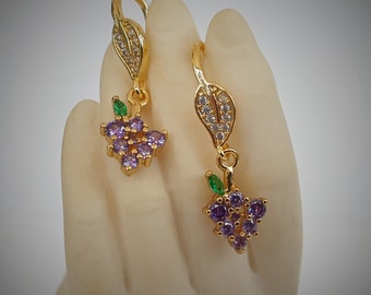 Könnte beinhalten: Ein Paar goldene Ohrringe mit violetten und grünen Steinen. Die Ohrringe sind in Form von Trauben mit Blättern gestaltet.