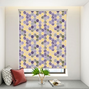 May include: A window blind with a geometric pattern of yellow and purple hexagons. The blind is partially rolled up, revealing a white wall behind it.