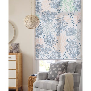 May include: A white roller shade with a blue and pink floral pattern. The shade is drawn down and the pattern is visible. The shade is in a room with a chair and a lamp.