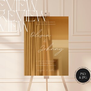 Puede incluir: Un letrero de boda dorado sobre un caballete. El letrero presenta los nombres "Olivia & Johnny" en escritura elegante, junto con los detalles del evento. El texto dice "Invite you to celebrate their love and marriage."