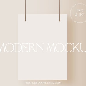 Puede incluir: Una maqueta de papel rectangular blanco suspendida por dos cuerdas marrones sobre un fondo beige. Las palabras "MODERN MOCKUP" se muestran en una fuente delicada. El texto "PSD & JPG" está en un círculo.