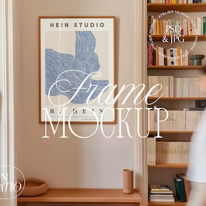 May include: A framed poster mockup featuring a minimalist design. The poster has a light background with a blue abstract design and the text "HEIN STUDIO". The frame is a warm brown color, and the overall aesthetic is modern and clean.