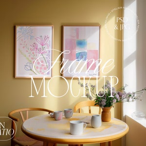 May include: A room setting with two framed art prints, one with floral and the other with abstract designs. A round table is set with mugs, a vase of flowers, and a wooden chair. The image includes the text "Frame Mockup" and "PSD & JPG".