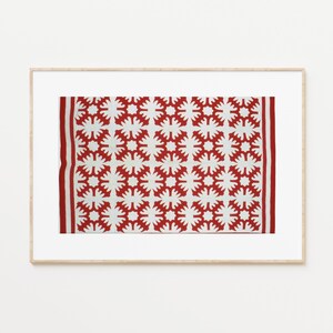 May include: A framed print of a red and white quilt with a geometric pattern of stars. The quilt is made of fabric and has a traditional design.