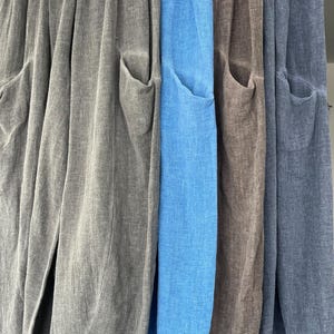 May include: Close-up of four pairs of linen trousers in shades of grey, blue, brown, and denim blue. Each pair features large front pockets. The fabric appears lightweight, suitable for warmer weather. The trousers are made of linen.