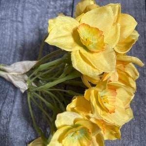 May include: A bunch of yellow daffodils with orange centers. The flowers are arranged in a bouquet and have green stems.