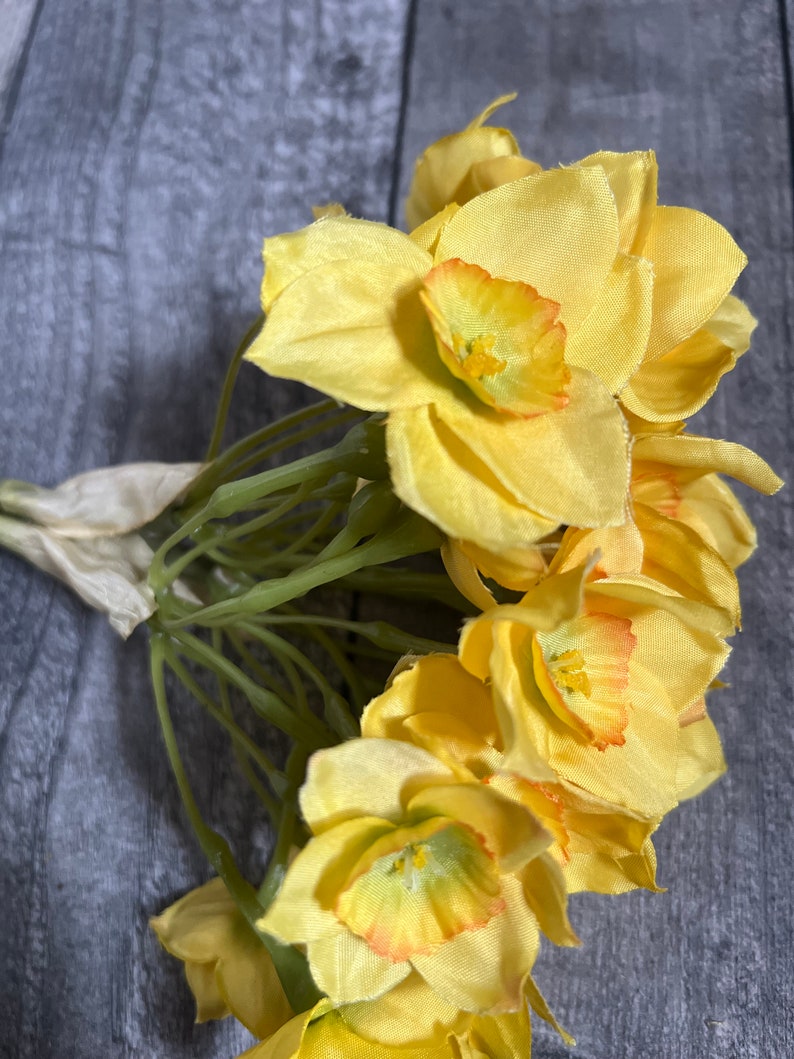 May include: A bunch of yellow daffodils with orange centers. The flowers are arranged in a bouquet and have green stems.