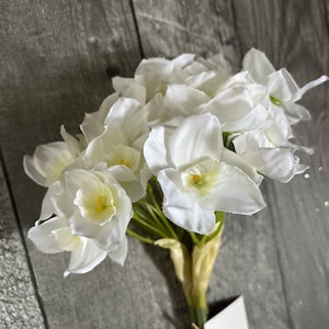 May include: A bouquet of white artificial daffodils with green stems. The flowers are arranged in a cluster and have a realistic appearance.