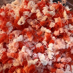 May include: A pile of red and white plastic decorative elements. The elements are in various shapes, including spirals and loops. The colors are vibrant, and the overall effect is visually interesting. These could be used for crafts or decorations.