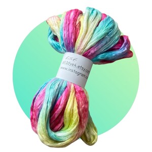 May include: A skein of hand-dyed silk ribbon in a rainbow of colours, including pink, yellow, blue, and green. The ribbon is tied with a white label that reads "Rose all2dye4.etsy.com www.instagram.com".