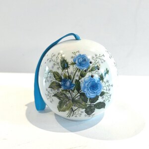 May include: A white ceramic ornament with a blue ribbon and a floral design featuring blue roses and green leaves.