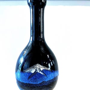 May include: A black ceramic vase with a blue and white glaze. The vase has a narrow neck and a round body.