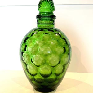 May include: A green glass bottle with a textured, bubble-like design and a decorative, pointed stopper.